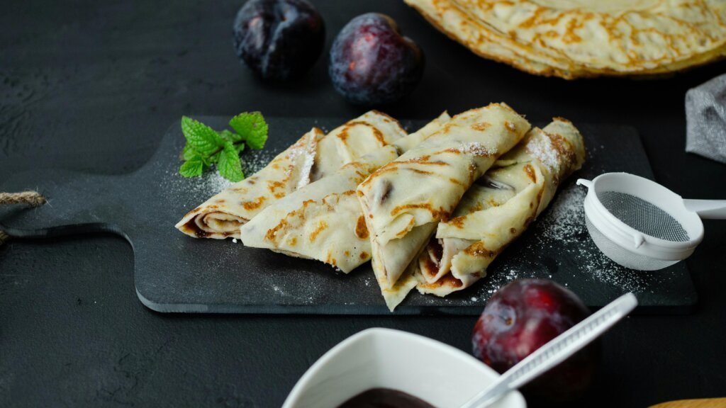 Crêpe au Nutella : le guide complet pour tout savoir 1 Delicious homemade crepes filled with jam and fresh plums on a serving board.