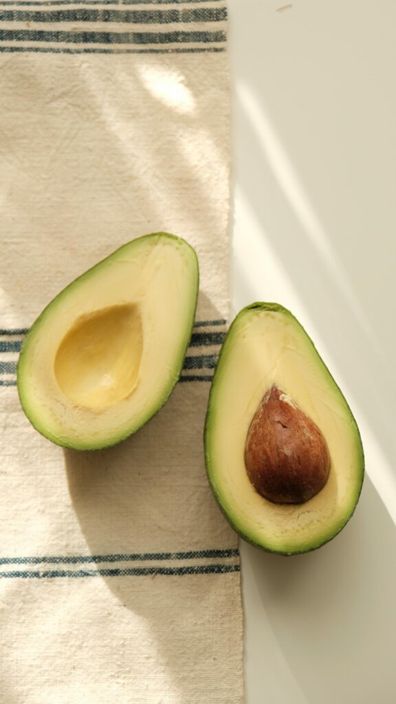 Régime Keto : Perdre du Poids 1 Sliced ripe avocado halves with pit on a rustic striped cloth, sunlight casts gentle shadows.